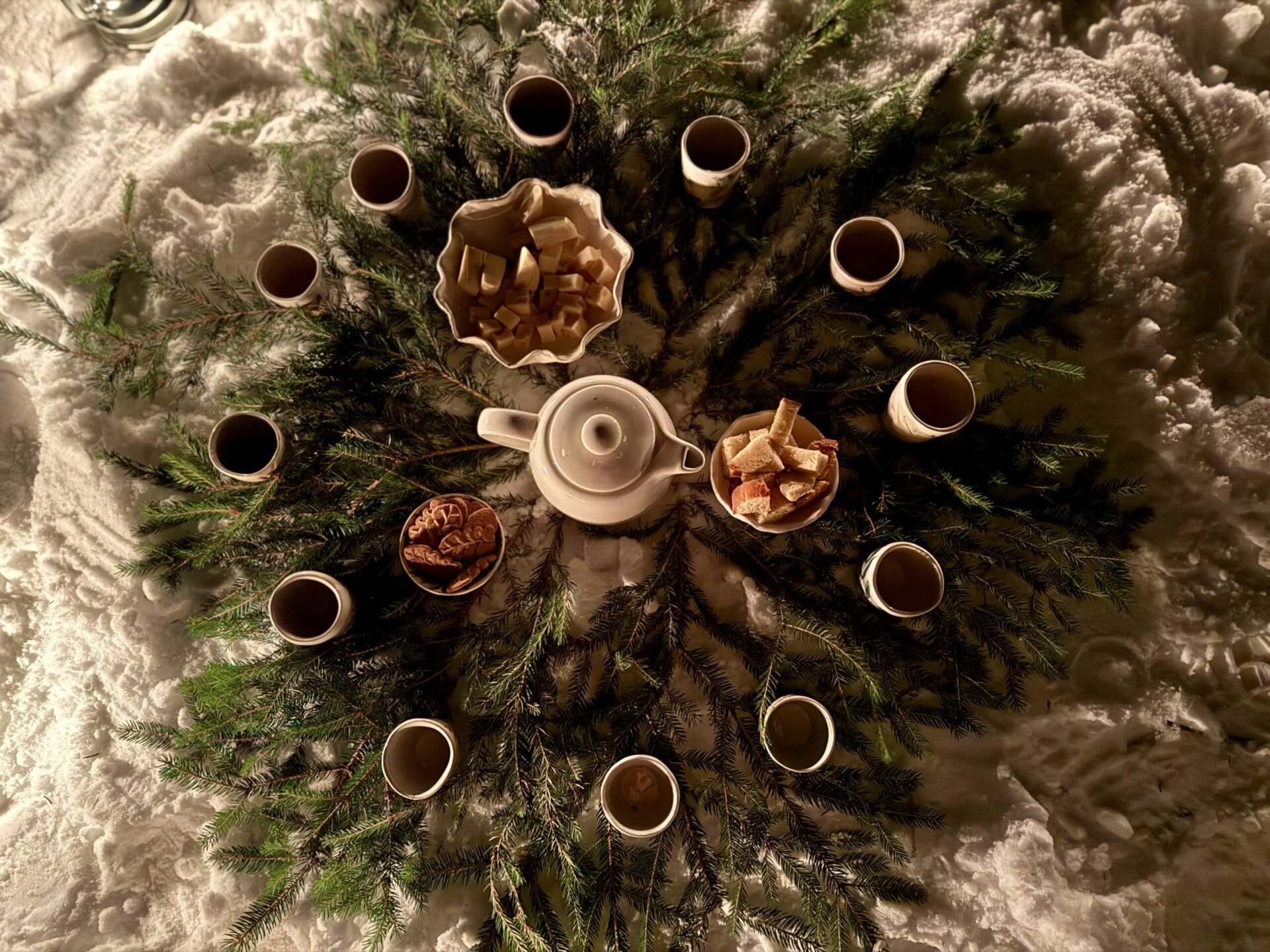 Cozy winter tea arrangement outdoors on pine branches with cups, teapot, and holiday treats in snow.